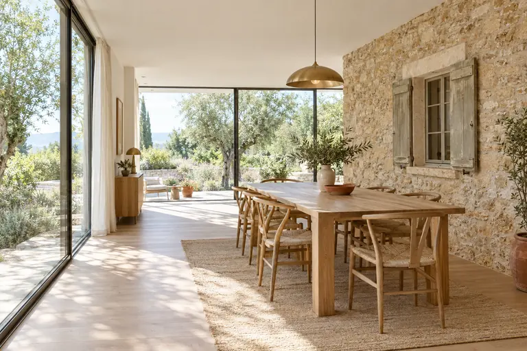 Intérieur d’une extension vitrée dont un mur est l’ancienne façade en pierre conservée avec sa fenêtre à volets