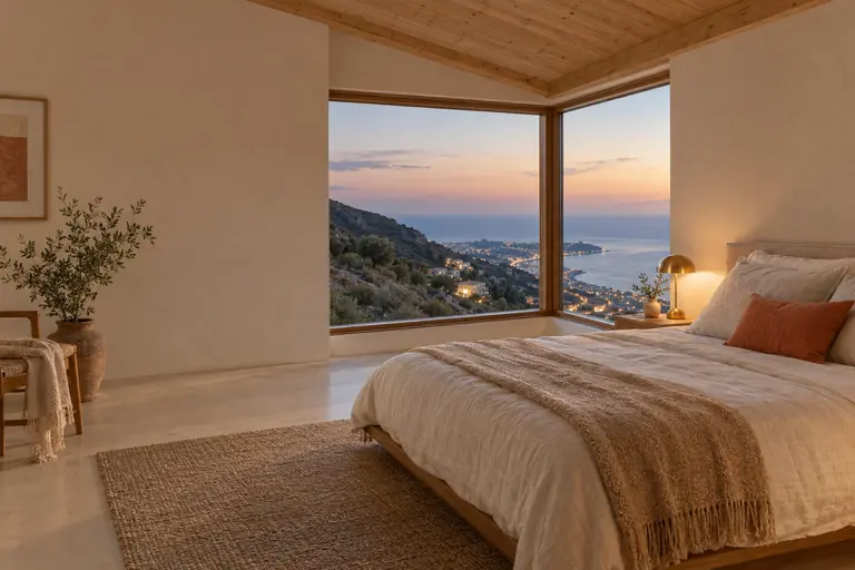 Chambre dans une extension sur pilotis au crépuscule, plafond bois et fenêtre d’angle ouverte sur la colline et la côte