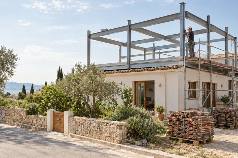 Ossature métallique d’un étage en cours de montage sur une maison de plain-pied, ouvrier de profil boulonnant une liaison
