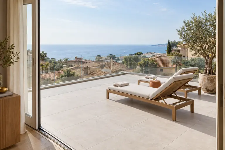 Toit-terrasse accessible sur une extension, dalles grises sur plots, garde-corps vitré et vue sur la mer au-delà des toits
