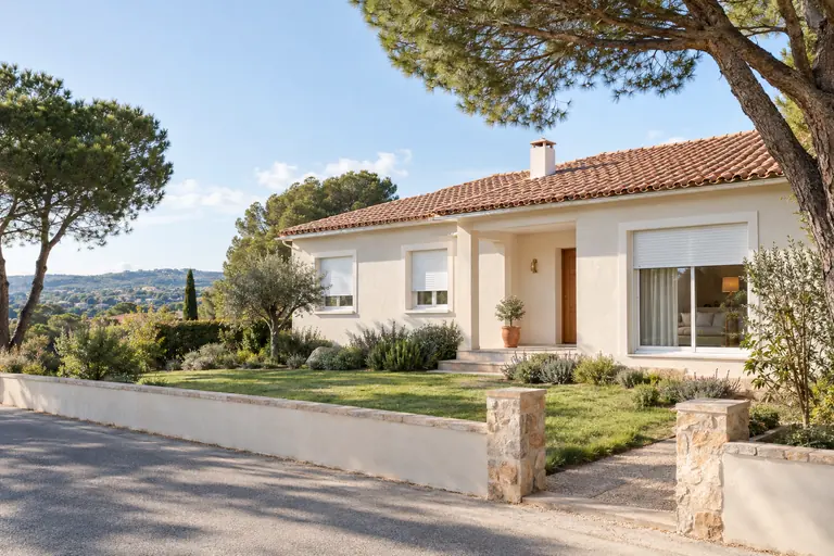 Pavillon de plain-pied des années 70 rénové avec enduit clair, volets roulants neufs et toiture en tuiles entre les pins