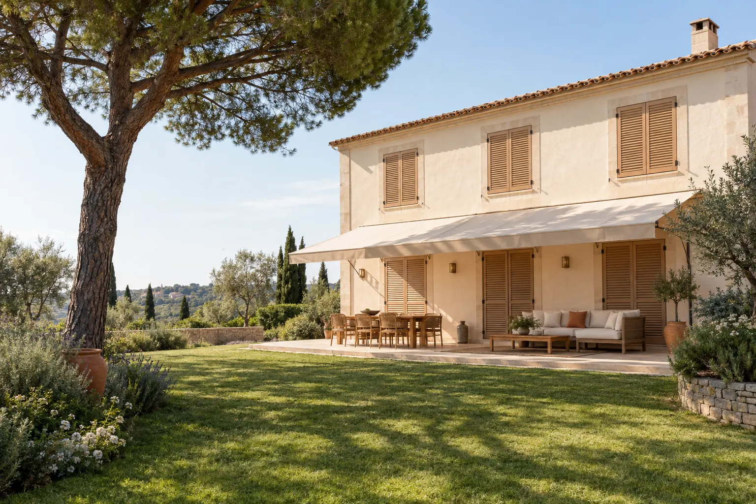 Façade ouest d’une villa varoise un après-midi d’été, persiennes bois fermées et store banne ombrageant la terrasse sous un pin