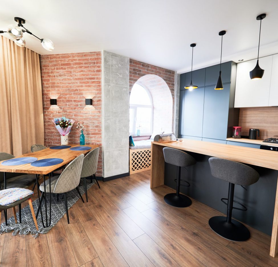 Living room and kitchen studio in dark blue color with modern furniture table, chair and stylish lamps. Concept of stylish modern interior kitchen with bar table.